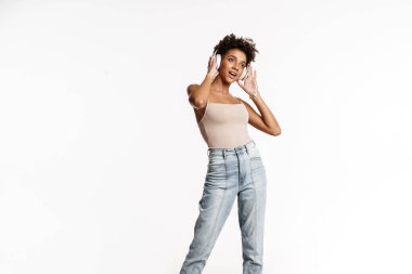 Young black woman in tank top listening music with headphones isolated over white background