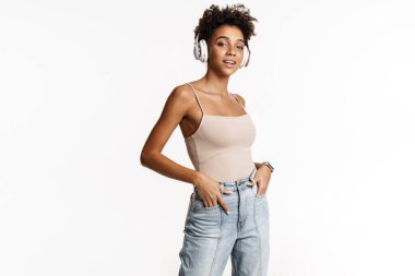 Young black woman in tank top listening music with headphones isolated over white background