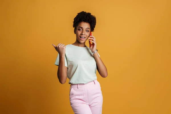 Young Black Woman Pointing Finger Aside While Talking Cellphone Isolated — Stockfoto