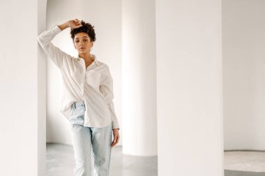 Young black woman leaning on wall and looking at camera indoors