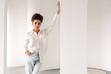 Young black woman leaning on wall and looking at camera indoors