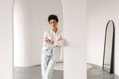 Young black woman leaning on wall and looking at camera indoors