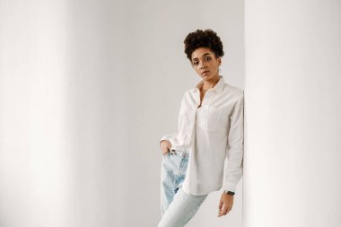 Young black woman leaning on wall and looking at camera indoors