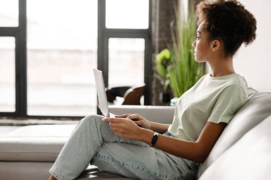 Young black woman working with laptop while sitting on couch at home