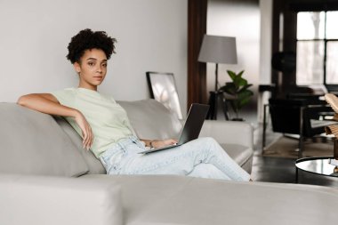 Young black woman working with laptop while sitting on couch at home