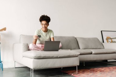 Young black woman using credit card while working with laptop at home