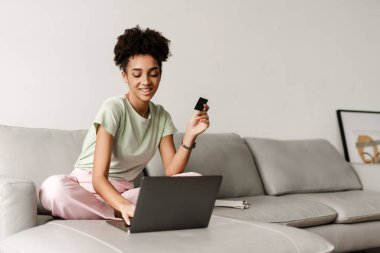 Young black woman using credit card while working with laptop at home
