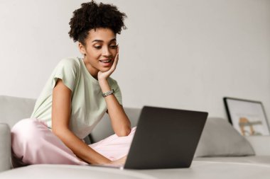 Young black woman working with laptop while sitting on couch at home