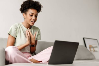 Young black woman gesturing and using laptop while sitting on couch at home