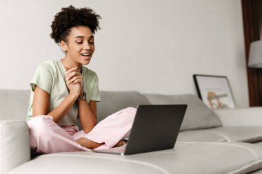 Young black woman gesturing and using laptop while sitting on couch at home