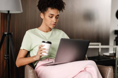 Young black woman drinking coffee while working with laptop at home