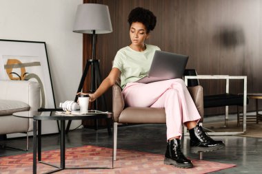Young black woman drinking coffee while working with laptop at home