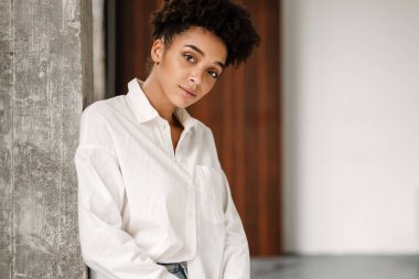 Young black woman leaning on wall and looking at camera indoors