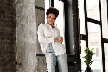 Young black woman leaning on wall and looking at camera indoors