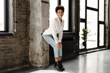 Young black woman leaning on wall and looking at camera indoors