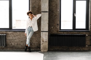 Young black woman leaning on wall and looking at camera indoors