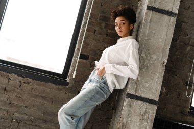 Young black woman leaning on wall and looking at camera indoors