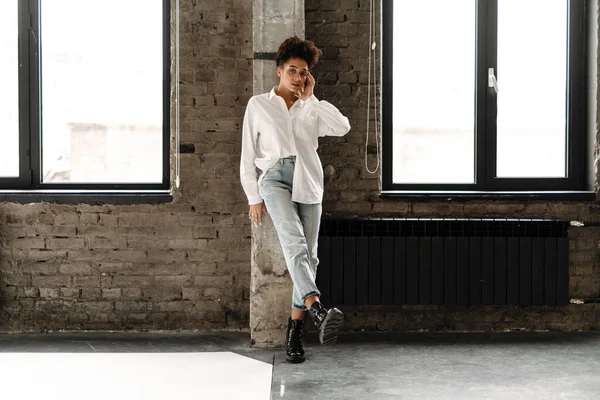 Young black woman leaning on wall and looking at camera indoors