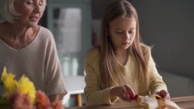 Kendine güvenen kız muz keser ve mutfakta büyükannesiyle konuşur.