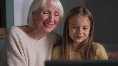 Büyükannesiyle birlikte gülümseyen kız evdeki tabletten video ile konuşuyor.