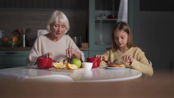 正の祖母と孫娘は朝食を食べてキッチンで話す — ストック動画