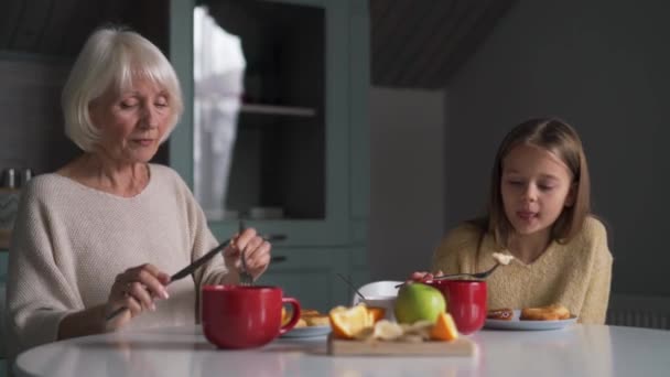 Skrattande Mormor Och Barnbarn Äter Frukost Och Pratar Köket — Stockvideo