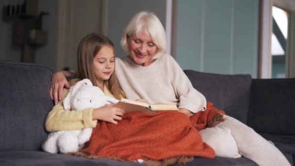 Happy Girl Her Grandmother Reading Book Sofa Home — Vídeo de Stock