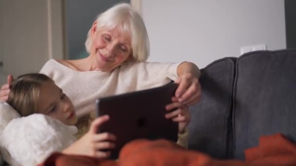Cheerful Grandmother Stroking Her Granddaughter Head Watching Something Tablet While — стоковое видео