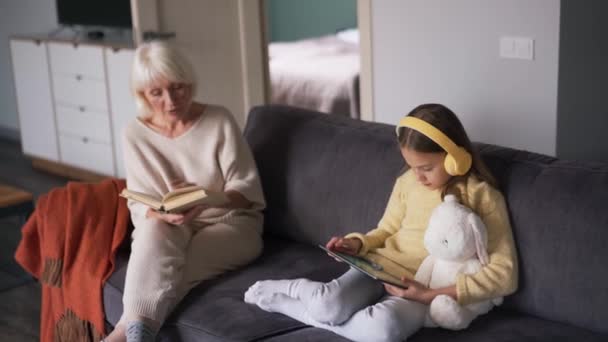 Overhead View Girl Headphones Looking Tablet While Her Grandmother Reading — Vídeo de Stock