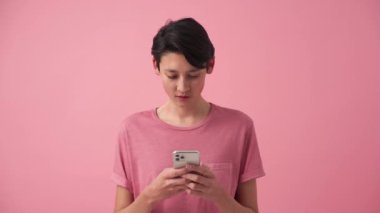 Gülümseyen Asyalı adam pembe stüdyoda telefonla mesaj atıyor.