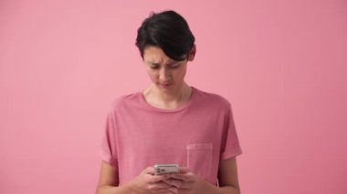 Memnun olmayan Asyalı adam pembe stüdyoda telefonla mesajlaşıyor.