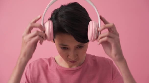 Cheerful Asian Man Putting Headphones Pink Studio — Vídeo de stock