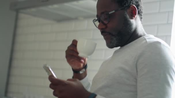 Όμορφος Αφρικανός Που Κοιτάζει Τηλέφωνο Ένα Φλιτζάνι Καφέ Στο Σπίτι — Αρχείο Βίντεο