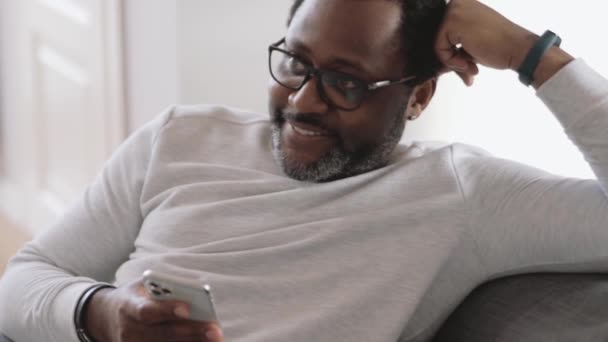 Sonriente Hombre Africano Viendo Televisión Hojeando Cinta Teléfono Casa — Vídeo de stock