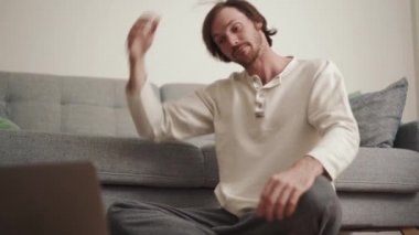 Concentrated long-haired man doing stretching according to the video tutorial at home