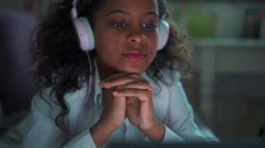Pretty African young girl with headphones watching something on laptop at home