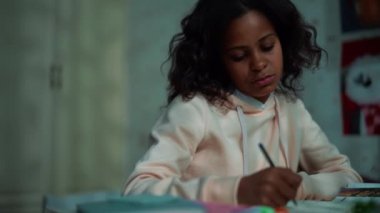 Bored African young girl doing homework and yawning at home