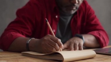 African man writing something from laptop in office