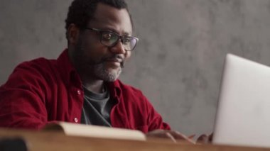 Smiling African man writing something from laptop in office