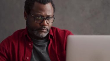 African man writing something from laptop and rejoicing in office