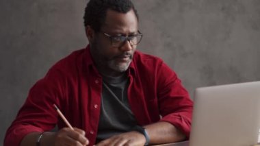 Serious African man writing something from laptop and rejoicing in office