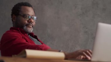 Smiling African man looking at phone and laptop in office