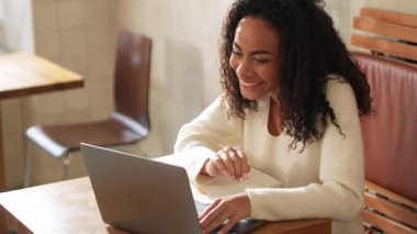 Smiling African woman talking by video call on laptop in cafe