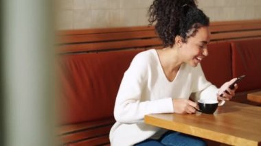 Laughing African woman looking at phone in cafe
