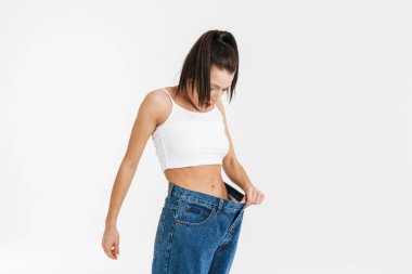 European brunette shocked woman posing in big jeans isolated over white background