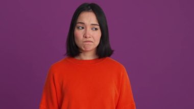 Kırmızı kazaklı bir kadın mor stüdyodaki kameraya bakıyor.