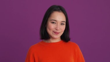 Mor stüdyodaki kameraya bakan gülen kadın.