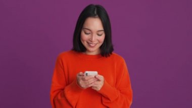 Mor stüdyoda telefonda yazan kırmızı kazaklı, gülen kadın.