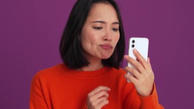 Kırmızı kazaklı yakışıklı bir kadın mor stüdyodaki kamerada görüntüsünü düzeltiyor.