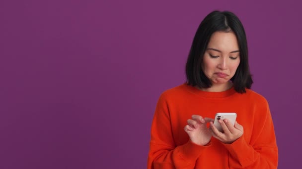 在紫色工作室里穿着红色毛衣在电话里打字的令人惊讶的女人 — 图库视频影像